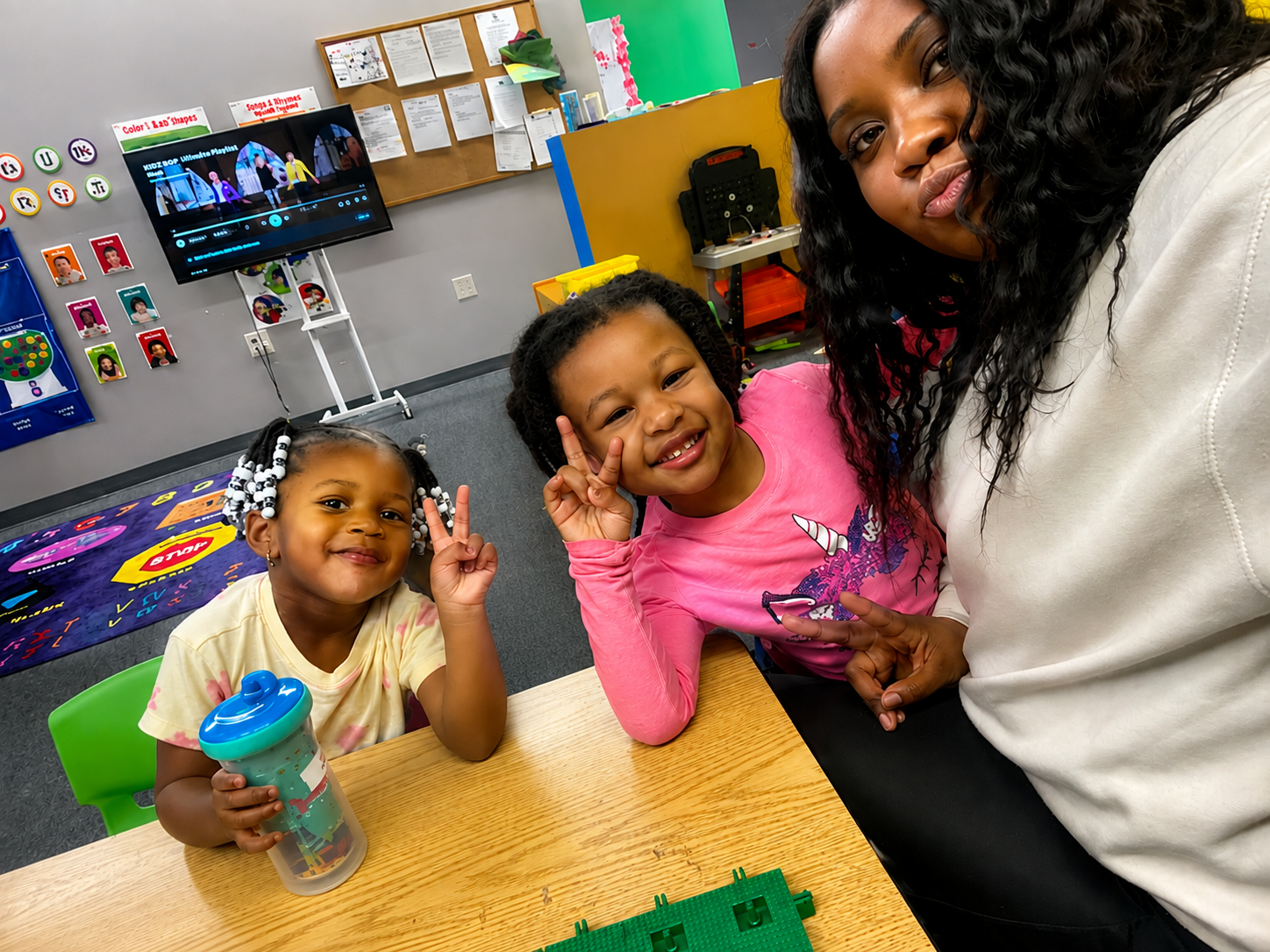 A caring teacher smiling with two happy preschoolers at a classroom table