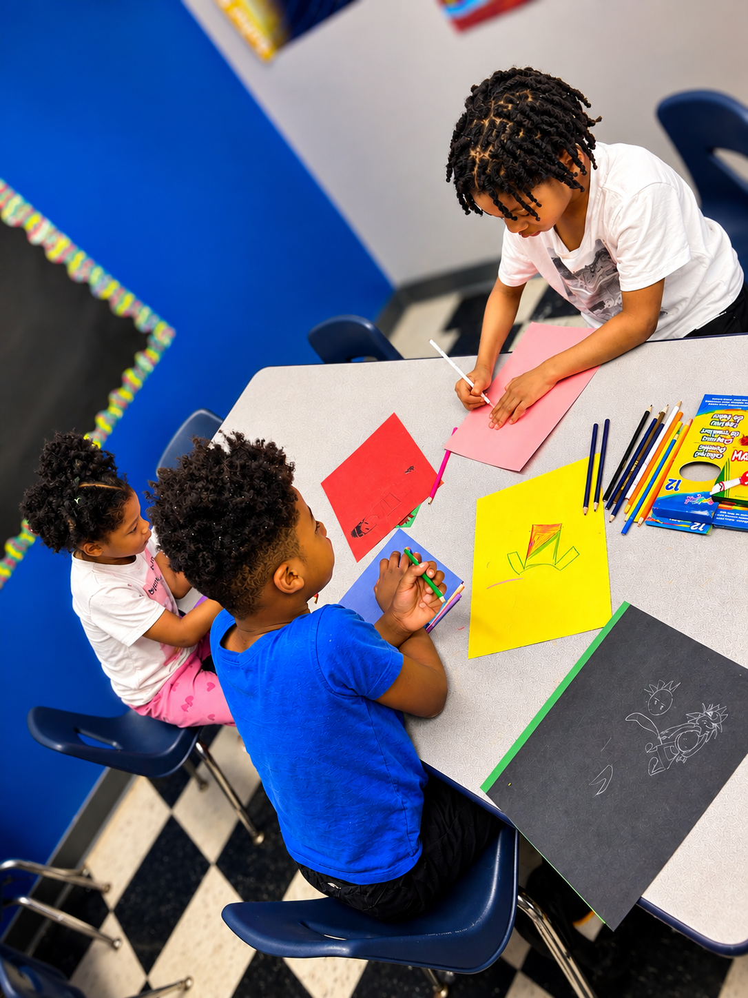 Children drawing on colored construction paper with pencils and markers