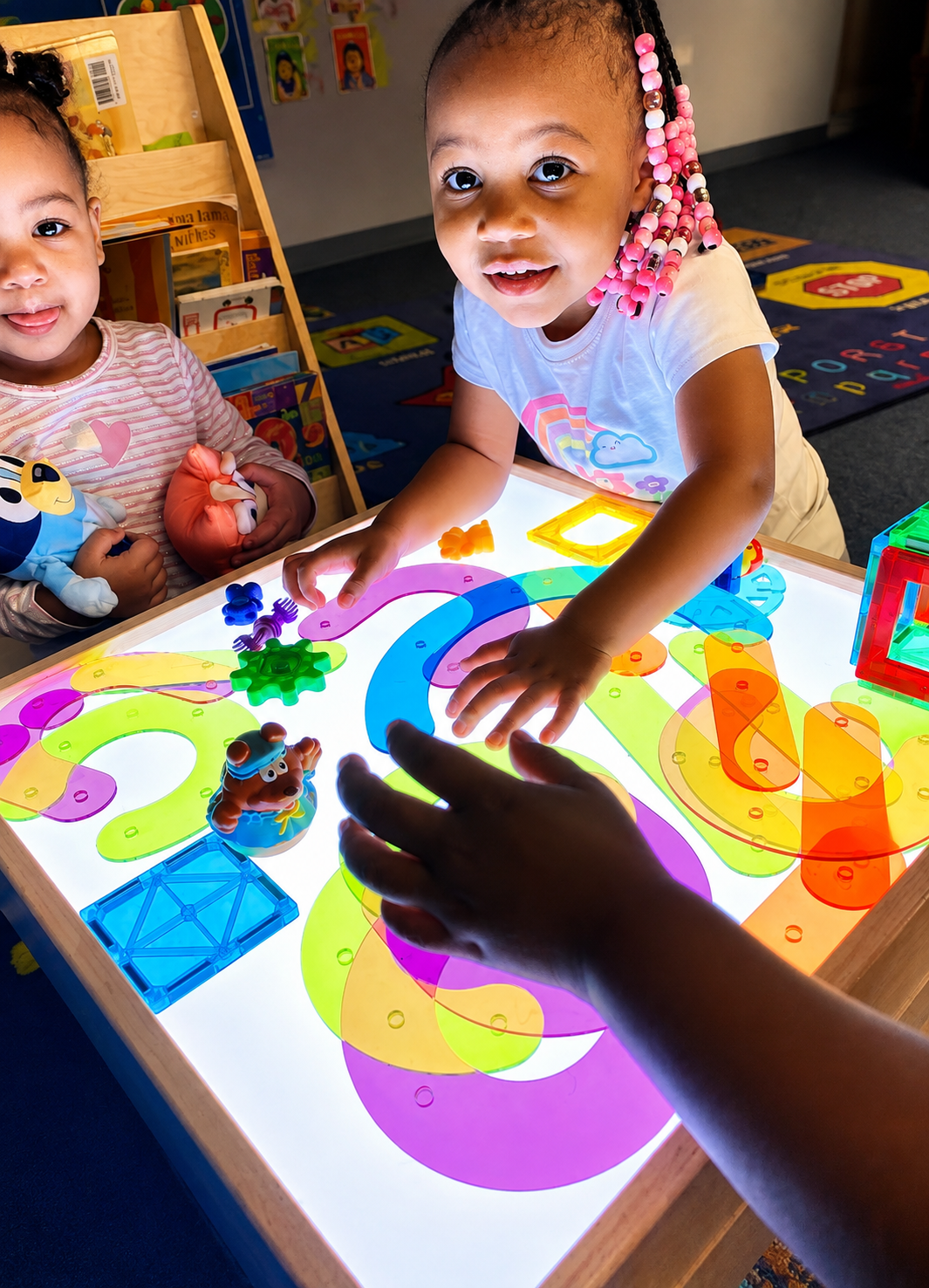 Toddlers arranging colorful translucent shapes on a glowing light table